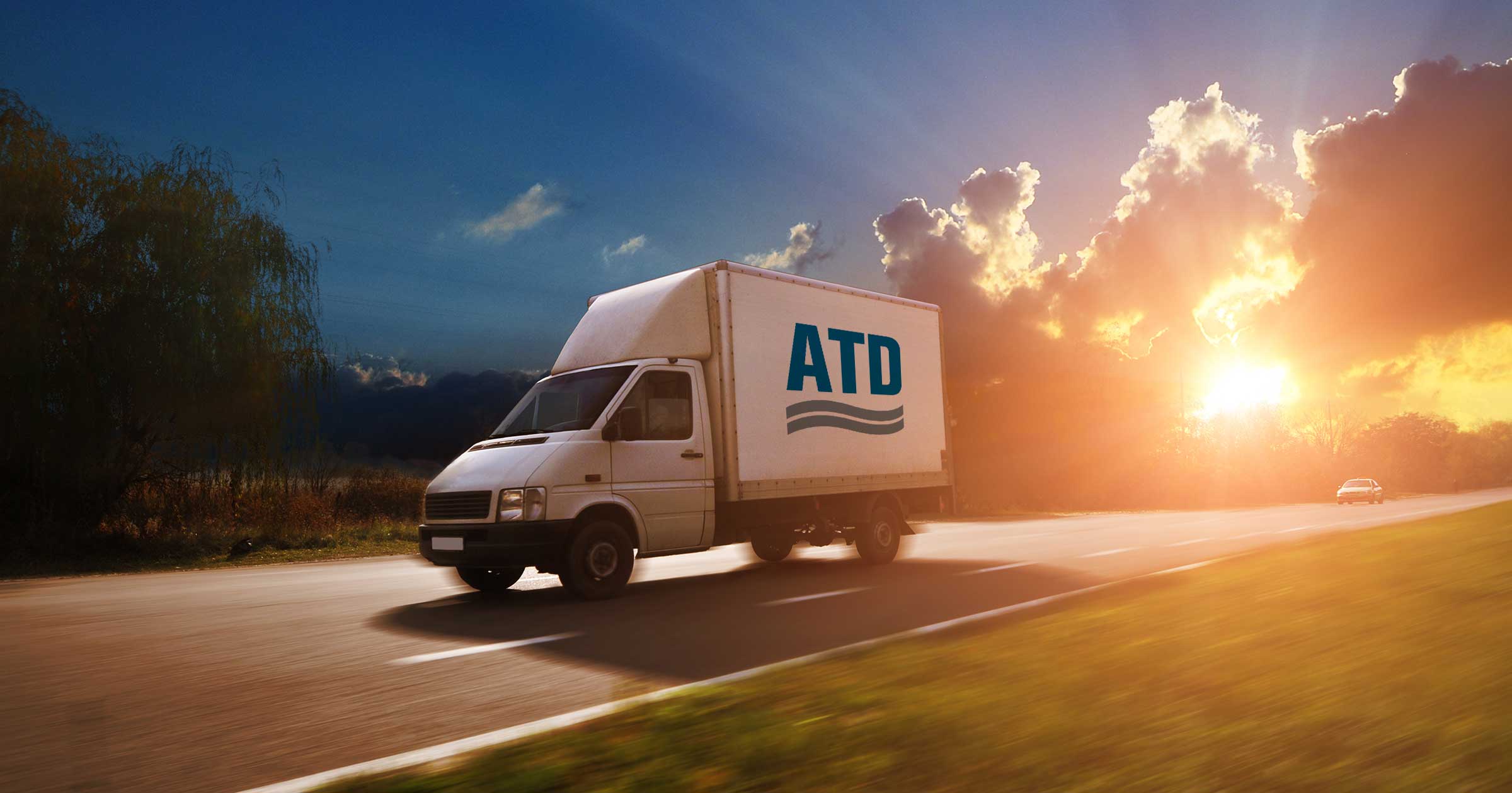 A commercial box truck drives on the highway at sunset